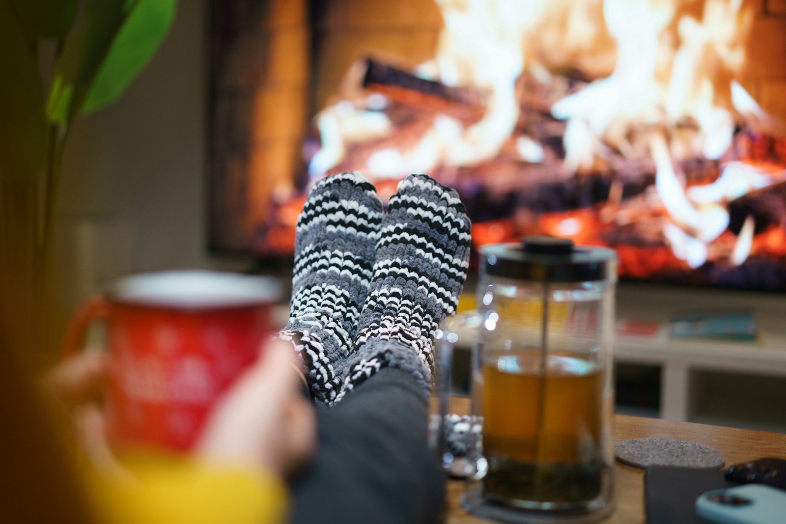 Feet in knit socks in front of a fireplace with tea and a red mug