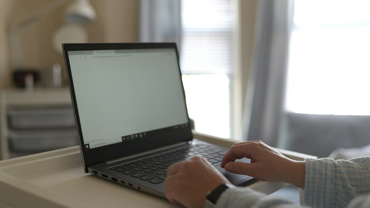 Person working on a laptop at a home desk by a window